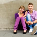 Teenager girl and boy sitting by wall