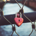 Close up of two red heart shaped padlocks locked together on a bridge railing